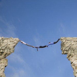 Businessmen holding hands and feet to bridge cliffs